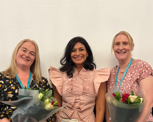 A photo of the two winners of the 2025 Gary Logue Awards with Dr Anisha Patel. Anisha is stood in the middle of the image with the winners, Rachel (left) and Charlotte (right) either side of her. Both Rachel and Charlotte are holding bunches of flowers.