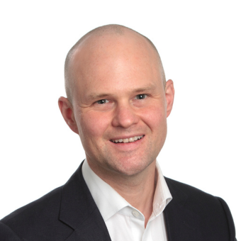 A photo of Dr James Whitworth smiling at the camera. He is wearing a white collared shirt and a black blazer. He has a plain white background behind him.