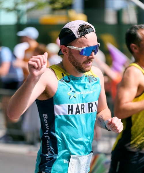 A photo of a runner taking on the Bournemouth Half Marathon. They are wearing a light teal branded running vest, a pair of white and blue sun glasses and a white and black cap. The runner is facing the right of the image and is giving a thumbs up to the camera.
