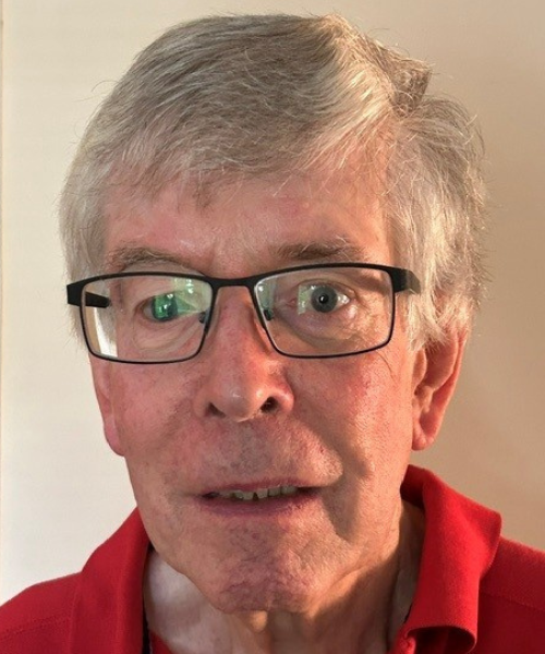 A headshot of Jim looking directly at the camera. They're wearing a red polo shirt and rectangular black-framed glasses. Their grey hair is combed to the left side.